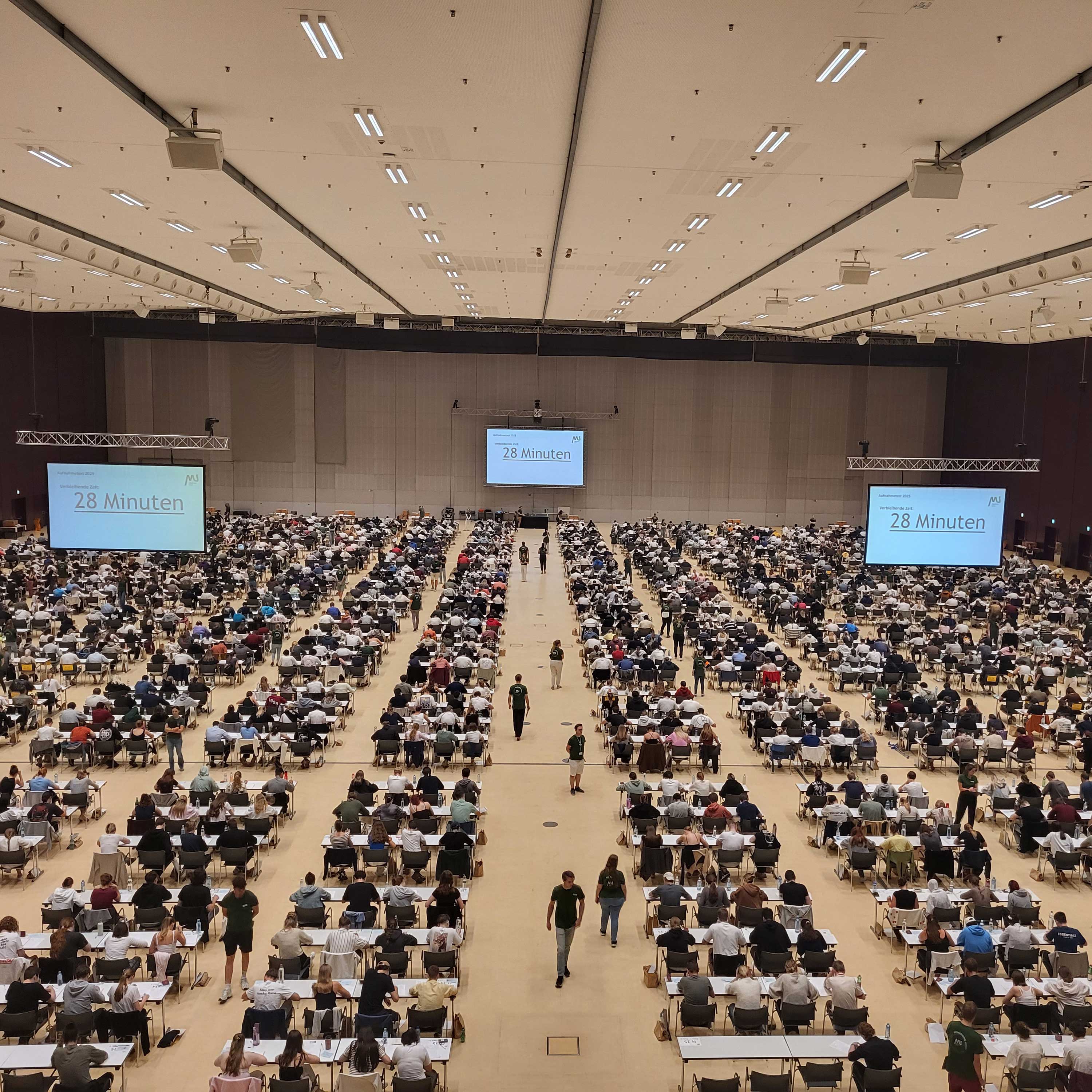 MedAT 2025 Teilnehmer*innen des MedAT 2025 sitzen in der Grazer Stadthalle an Tischen.